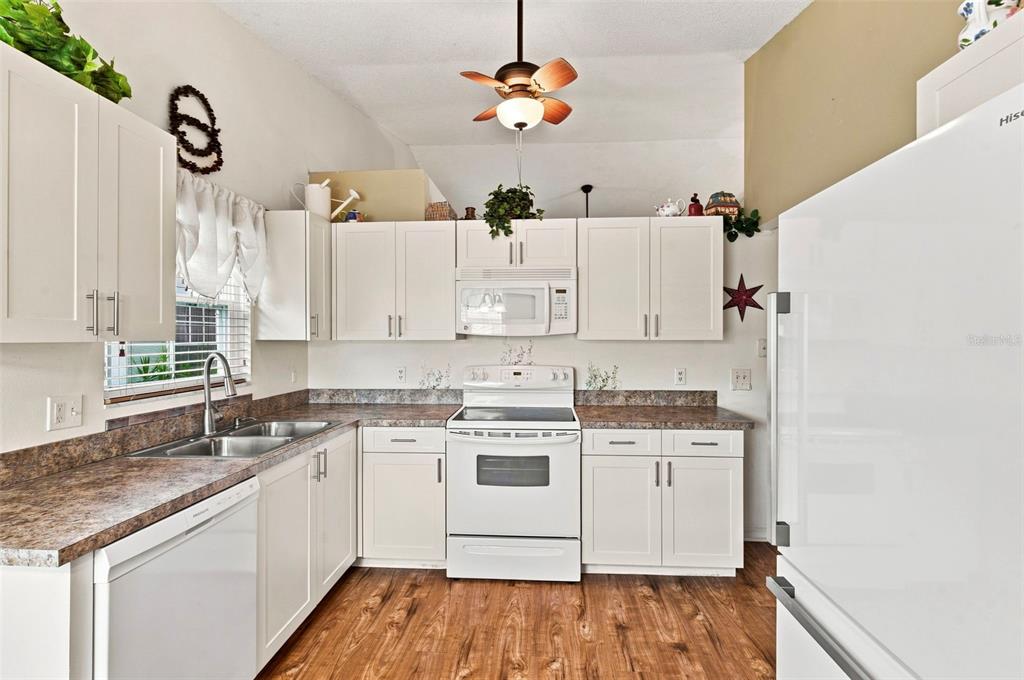 A kitchen features white cabinetry, a white stove, a double sink, and wood-look flooring — 7637 BALHARBOUR DRIVE, NEW PORT RICHEY, FL