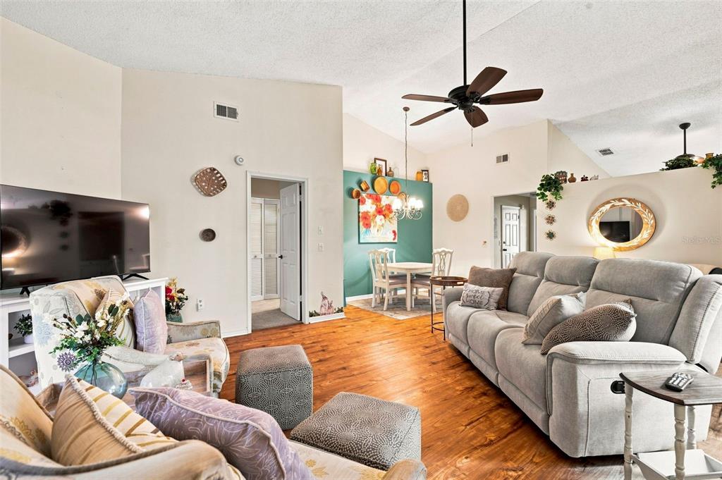 A living room with wood floors, a gray sofa, a patterned armchair, and a dining area — 7637 BALHARBOUR DRIVE, NEW PORT RICHEY, FL