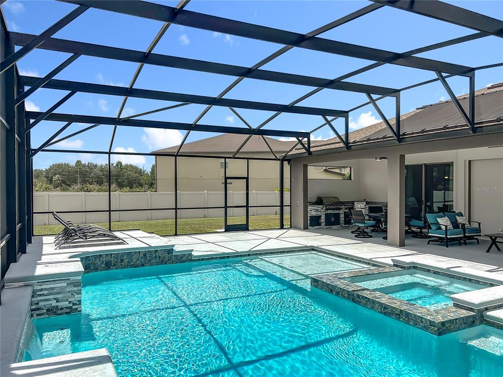 A screened-in pool area features a spa, lounge chairs, and an outdoor kitchen — 15084 CUDDY COURT, ORLANDO, FL