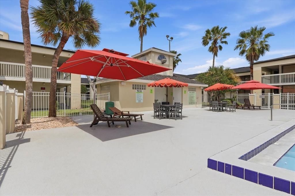 A pool deck features lounge chairs, tables with umbrellas, and palm trees near apartment buildings — 5245 W IRLO BRONSON MEMORIAL HIGHWAY UNIT 258, KISSIMMEE, FL