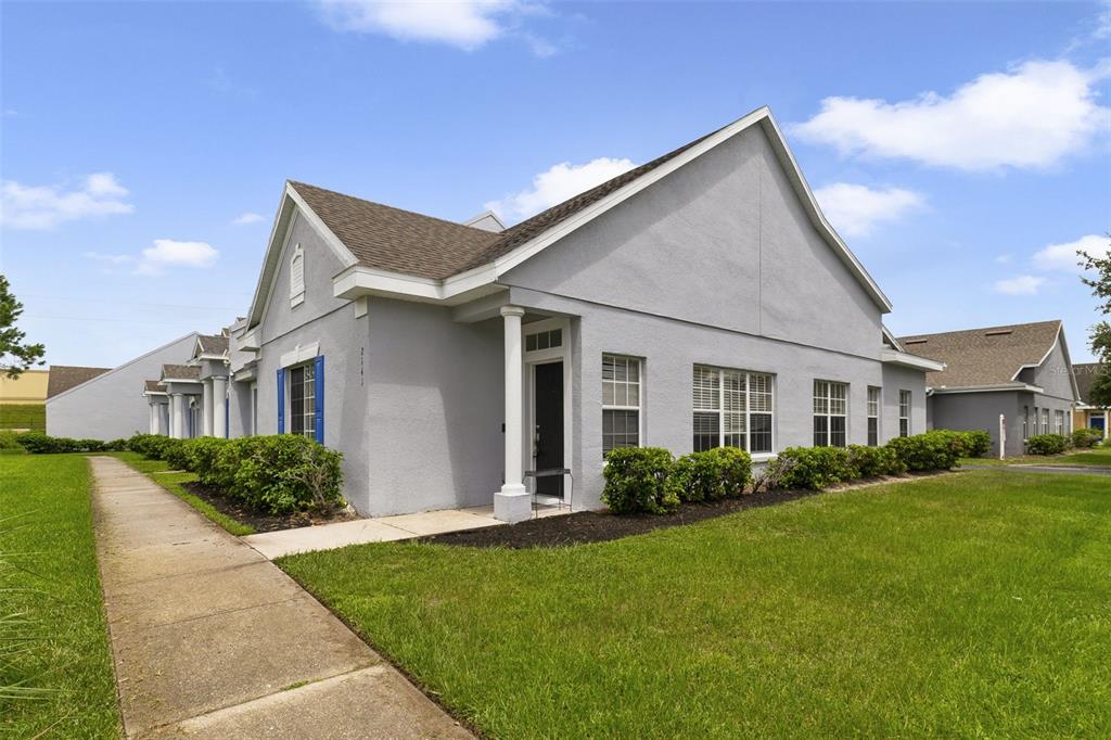 A gray, single-story residential building with a sidewalk, green lawn, and blue shutters — 2141 ISLAND WALK DRIVE, ORLANDO, FL