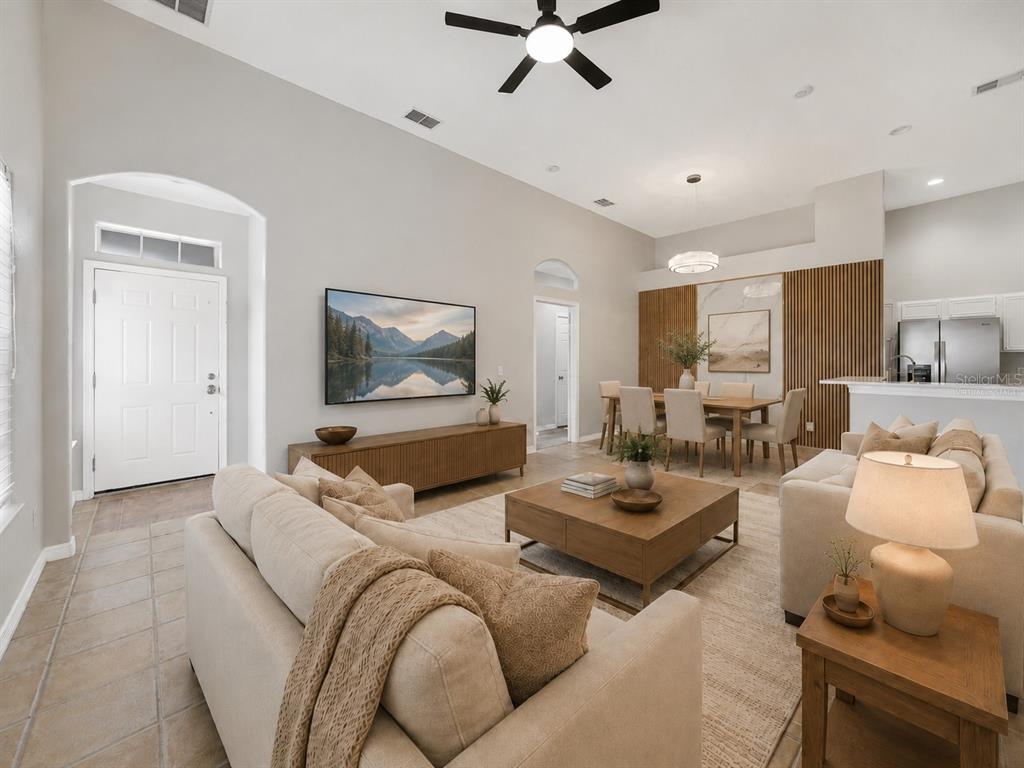 An open-concept living and dining area features vaulted ceilings, neutral furniture, and wood-slat wall accents — 2141 ISLAND WALK DRIVE, ORLANDO, FL