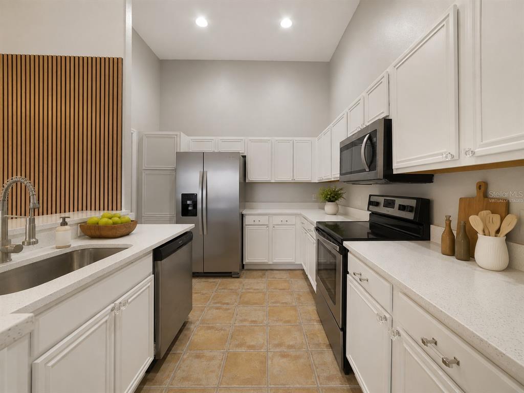 A kitchen with white cabinets, stainless steel appliances, quartz countertops, and tan tile flooring — 2141 ISLAND WALK DRIVE, ORLANDO, FL