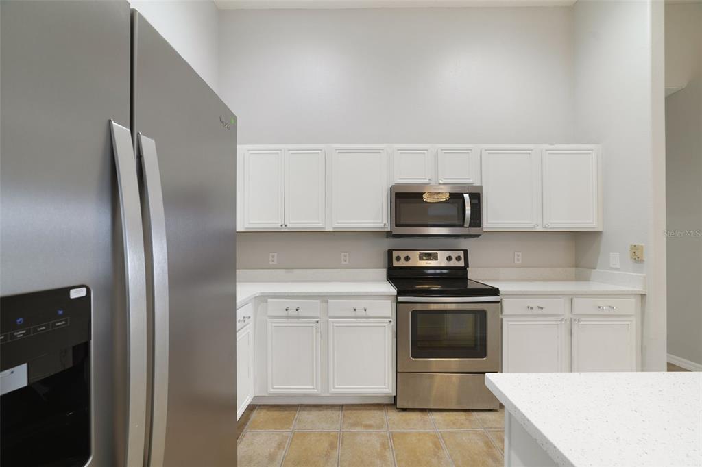 A kitchen features white cabinets, stainless steel appliances, and light-colored countertops — 2141 ISLAND WALK DRIVE, ORLANDO, FL