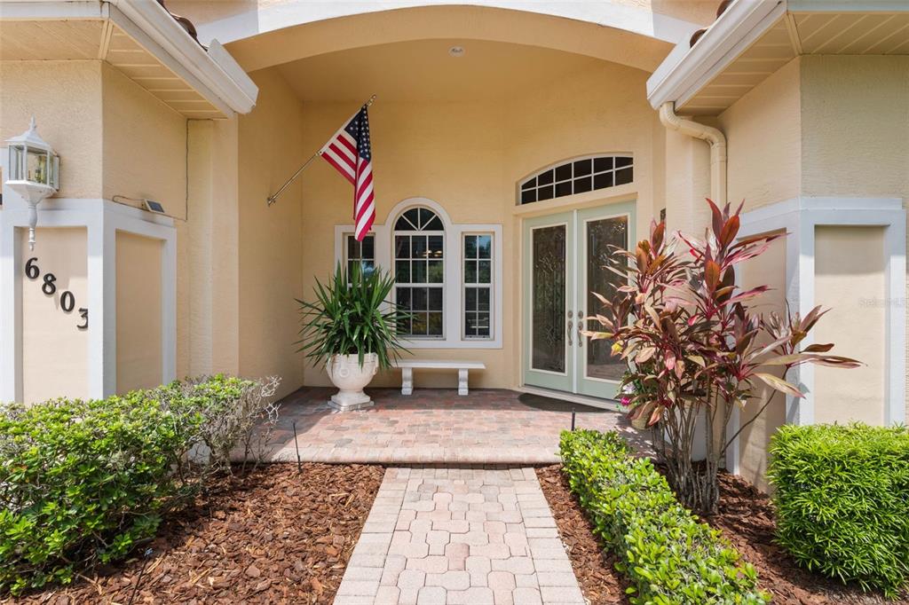The exterior entrance features a brick paver walkway, a double door, and an American flag — 6803 COYOTE RIDGE COURT, BRADENTON, FL
