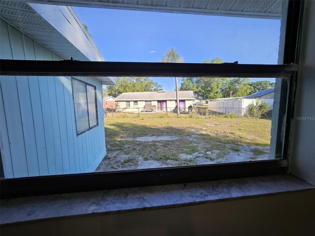 A view through a window shows a backyard with a neighboring house and fence — 6004 FORTUNE PLACE, APOLLO BEACH, FL