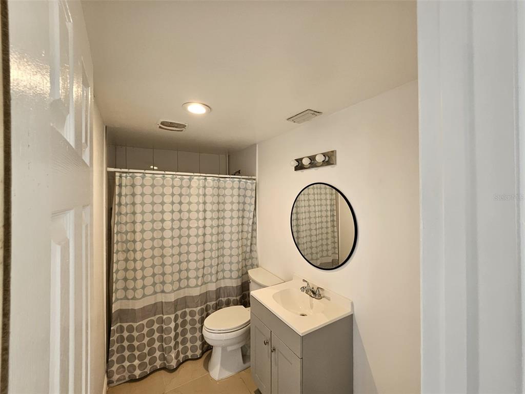 A bathroom features a gray vanity, a round mirror, and a shower with a patterned curtain — 6004 FORTUNE PLACE, APOLLO BEACH, FL