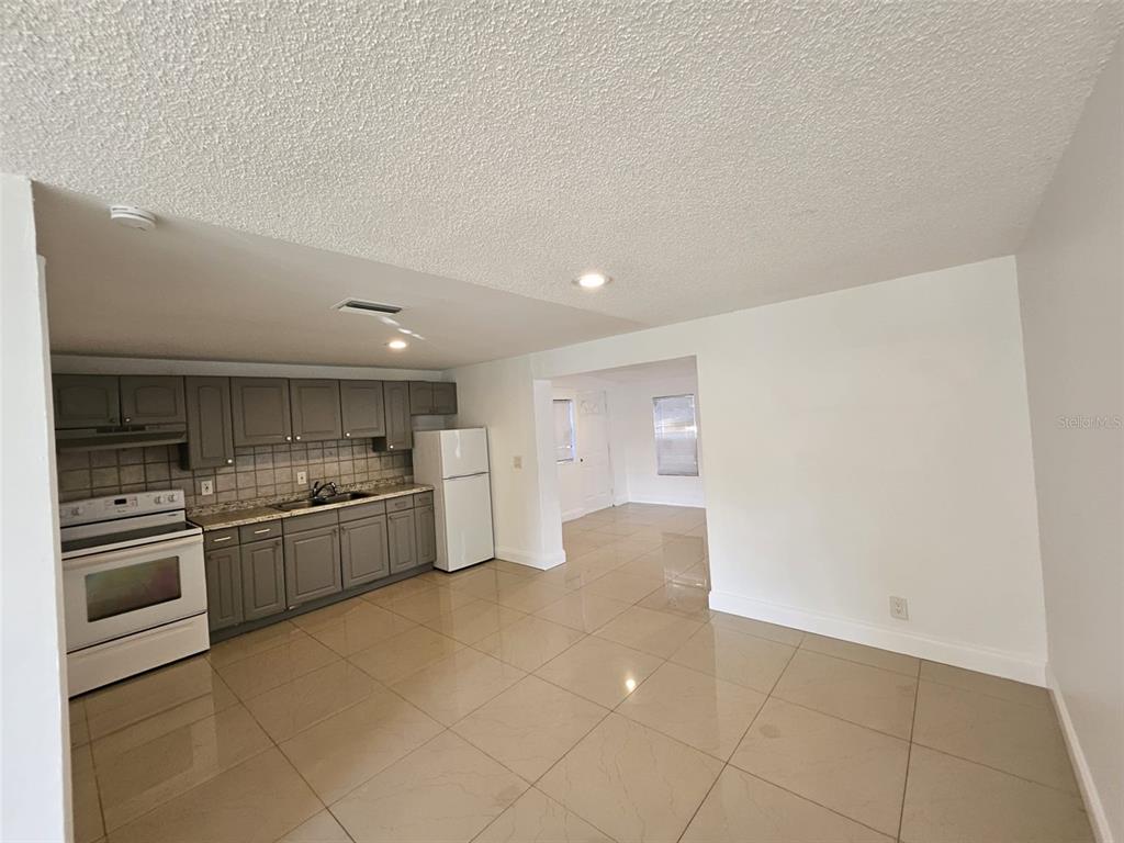 A kitchen with gray cabinets and tile flooring opens into an adjacent living area — 6004 FORTUNE PLACE, APOLLO BEACH, FL