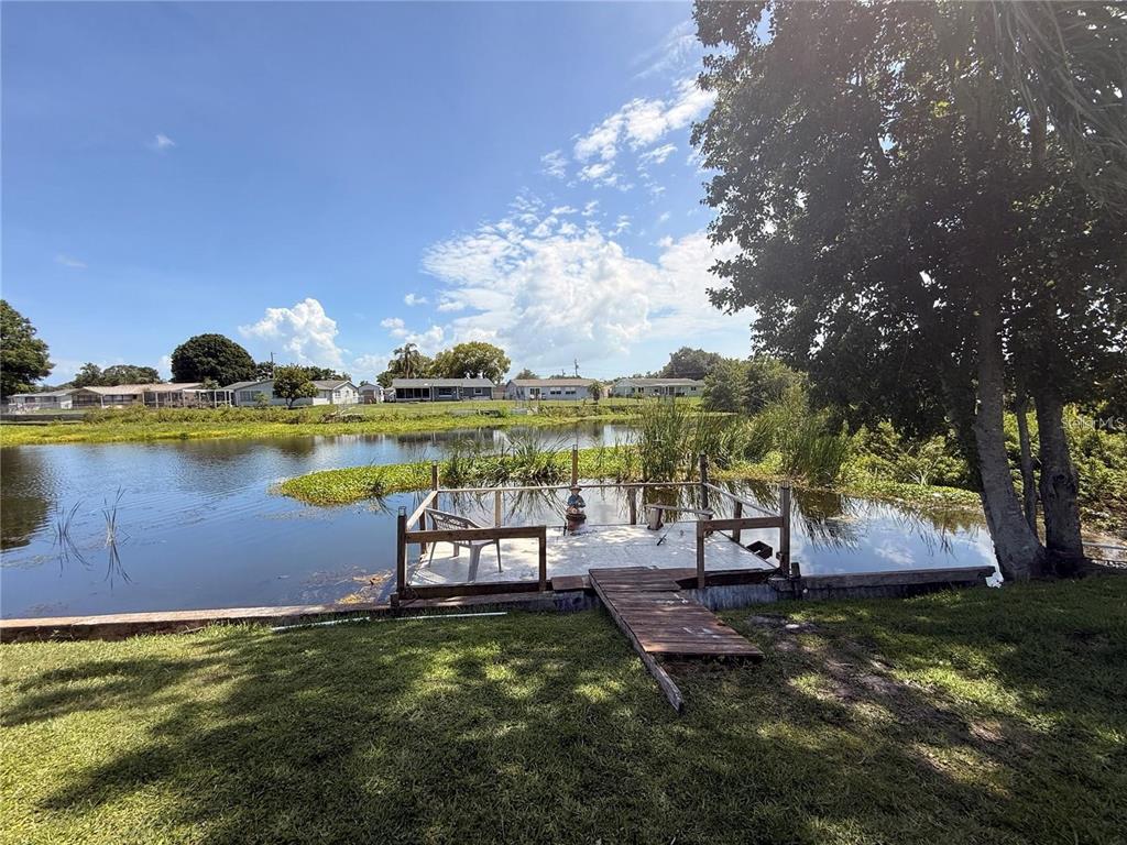 A wooden dock with a railing extends into a pond behind a grassy yard — 5144 CHIME WAY, HOLIDAY, FL