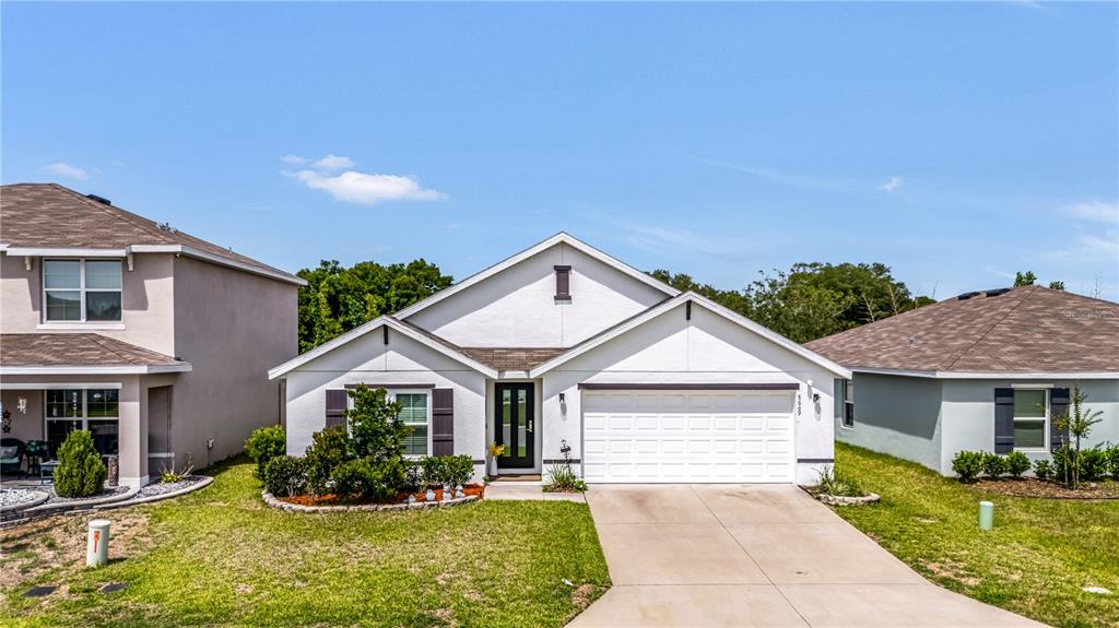 A single-story suburban house with a white exterior, dark shutters, and a two-car garage — 8669 TRIUMPH CIRCLE, WILDWOOD, FL