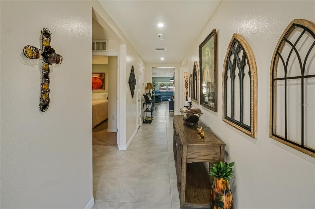 A hallway with tile flooring leads past a console table and wall decor toward a room — 8669 TRIUMPH CIRCLE, WILDWOOD, FL