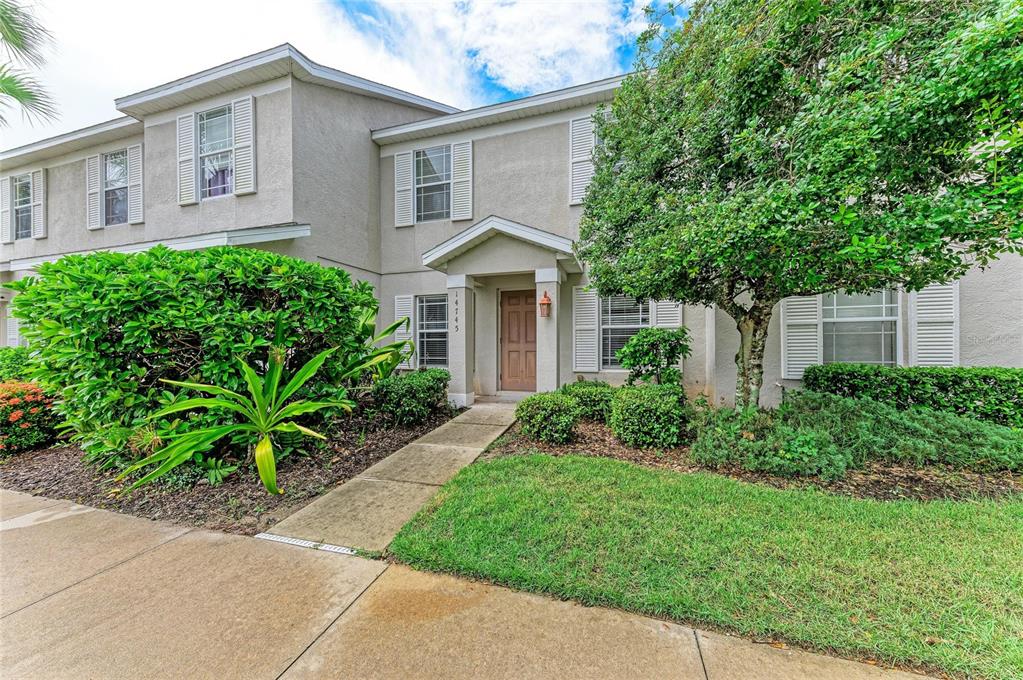 A two-story townhouse exterior with a tan door, concrete walkway, and landscaped front yard — 14745 AMBERJACK TERRACE UNIT 1, BRADENTON, FL
