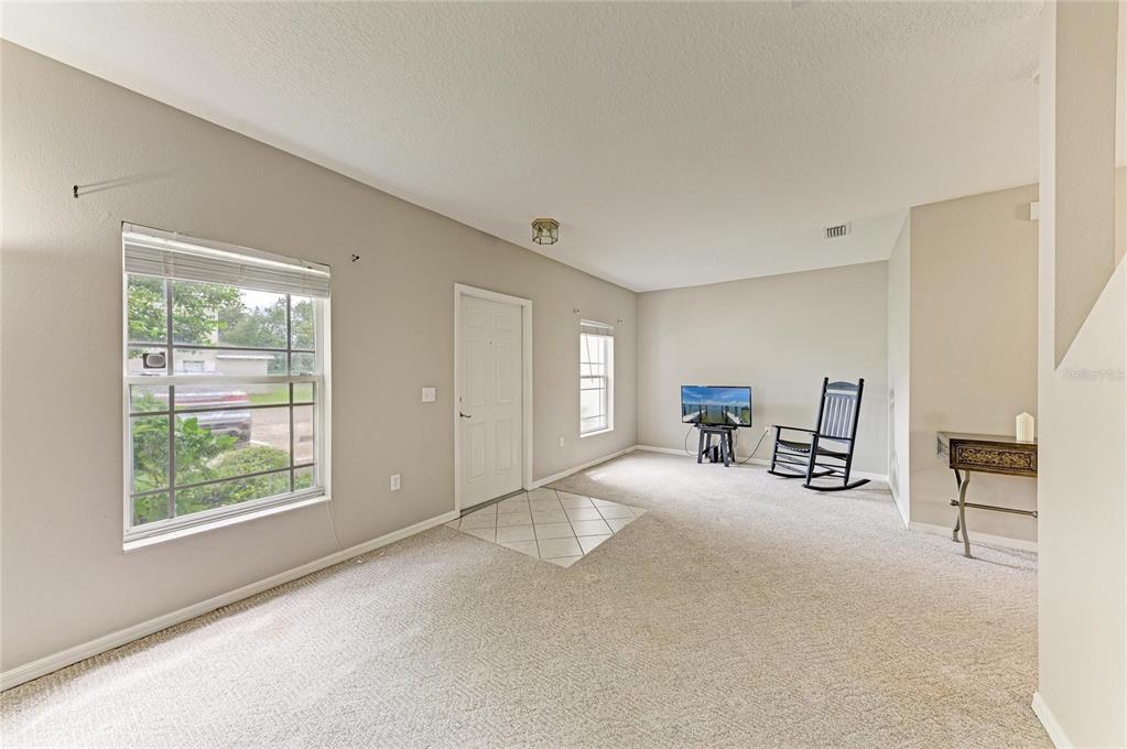 A living room with beige carpet, a front door, two windows, and a rocking chair — 14745 AMBERJACK TERRACE UNIT 1, BRADENTON, FL