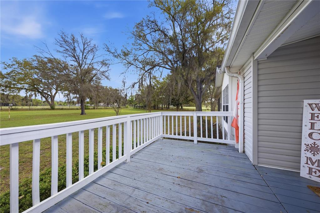 A wooden deck with white railings overlooks a grassy yard with large trees — 18850 SE 12TH LANE, WILLISTON, FL