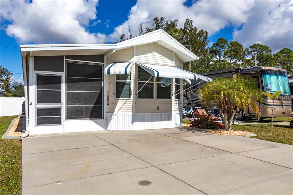 A single-story manufactured home with a screened porch and concrete driveway under a blue sky — 1604 N MANATEE LOOP, PUNTA GORDA, FL
