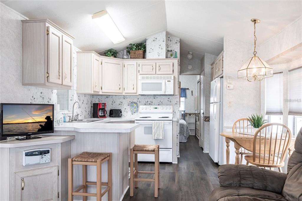 A kitchen with light wood cabinets, white appliances, and a breakfast bar with two stools — 1604 N MANATEE LOOP, PUNTA GORDA, FL