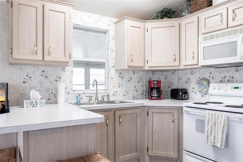 A kitchen with light wood cabinets, floral wallpaper, white countertops, and a white stove — 1604 N MANATEE LOOP, PUNTA GORDA, FL