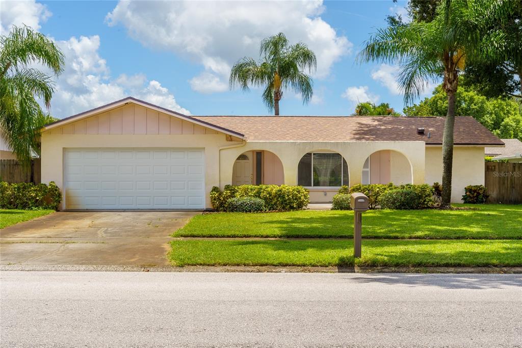 A single-story house with a two-car garage, arched entryway, and a palm tree-lined lawn — 2419 TIMBERCREST CIRCLE W, CLEARWATER, FL