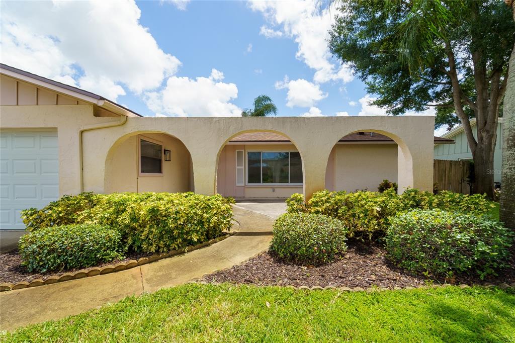 A single-story house exterior features a covered entryway with three arches and a concrete walkway — 2419 TIMBERCREST CIRCLE W, CLEARWATER, FL