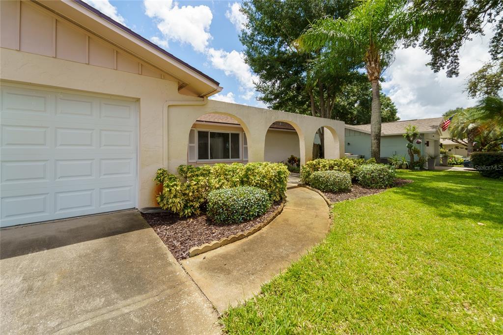 A beige house exterior features a garage, a curved walkway, and arched architectural details — 2419 TIMBERCREST CIRCLE W, CLEARWATER, FL