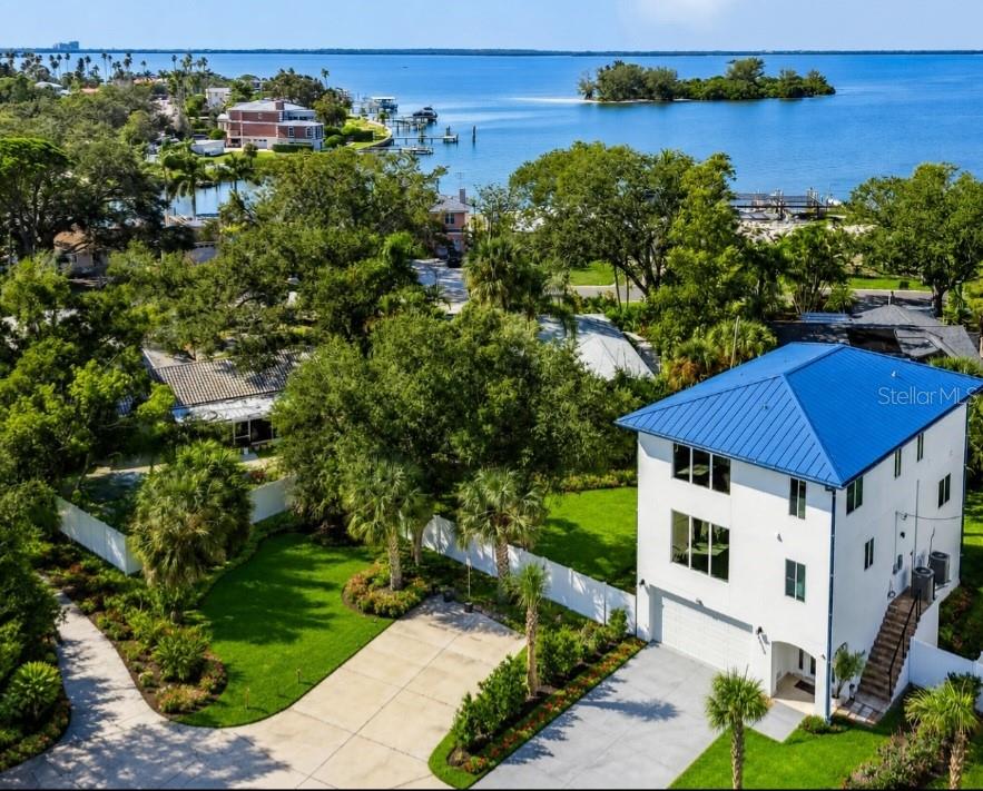 An aerial view of a white three-story house with a blue metal roof near water — 1956 CEDAR DRIVE, DUNEDIN, FL