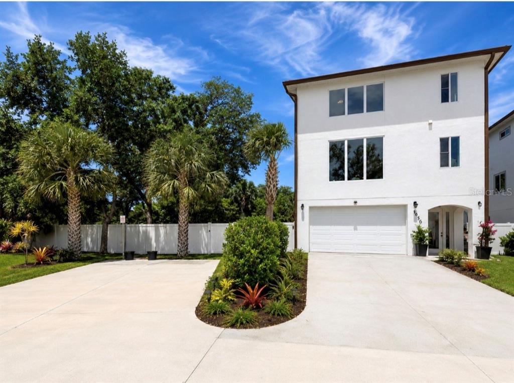A three-story white house with a two-car garage and a landscaped driveway — 1956 CEDAR DRIVE, DUNEDIN, FL