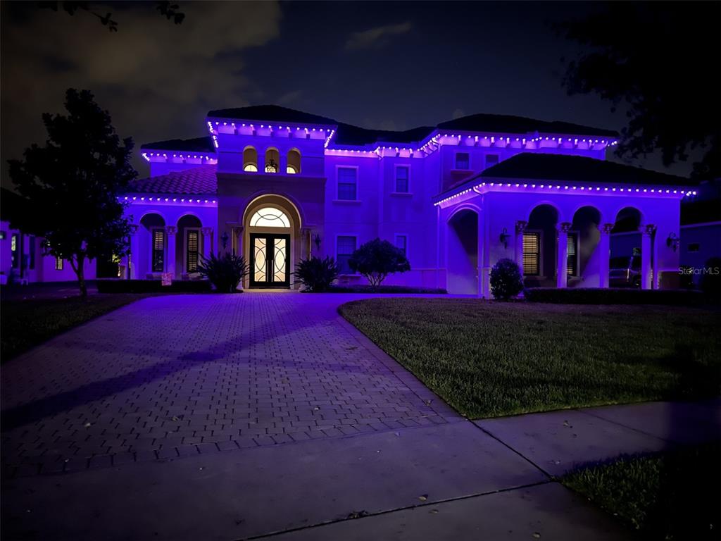 A large two-story house at night illuminated with purple exterior accent lighting — 5526 MARLEON DRIVE, WINDERMERE, FL