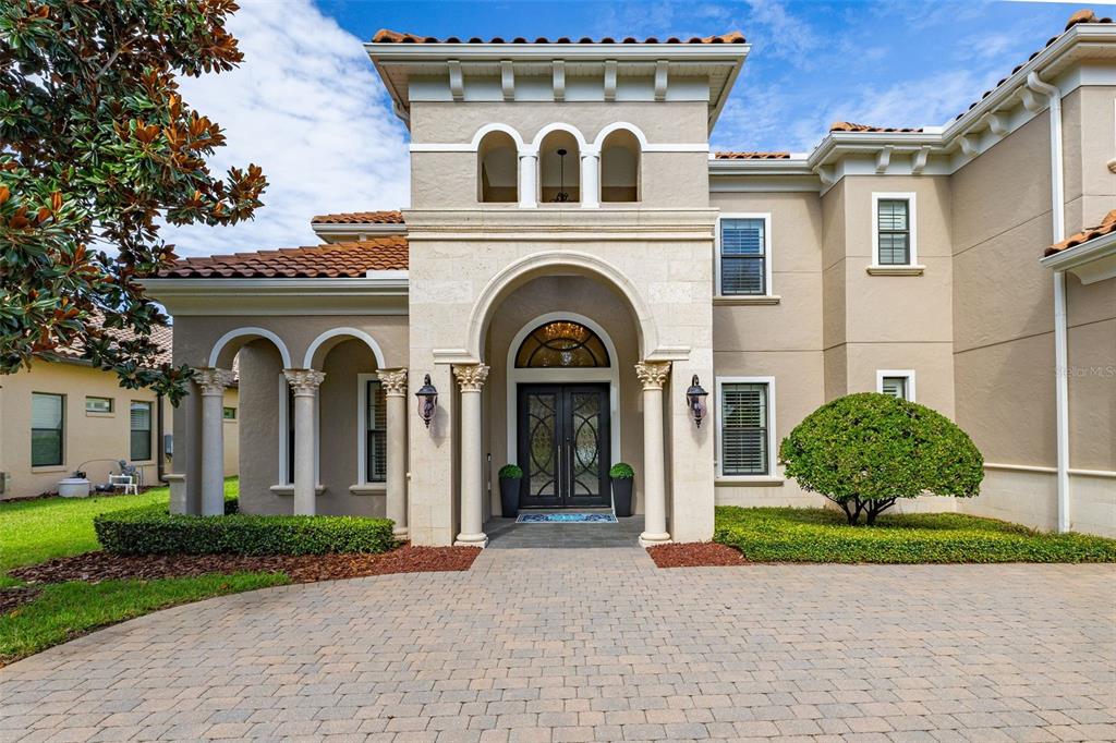 A two-story Mediterranean-style home features a stone arched entryway, columns, and a paved driveway — 5526 MARLEON DRIVE, WINDERMERE, FL