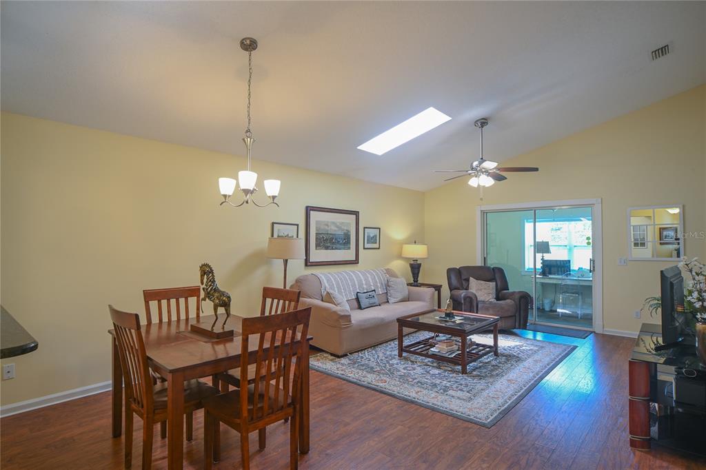 A living and dining room with hardwood floors, a vaulted ceiling, and a sliding glass door — 1918 NW 50TH AVENUE, OCALA, FL