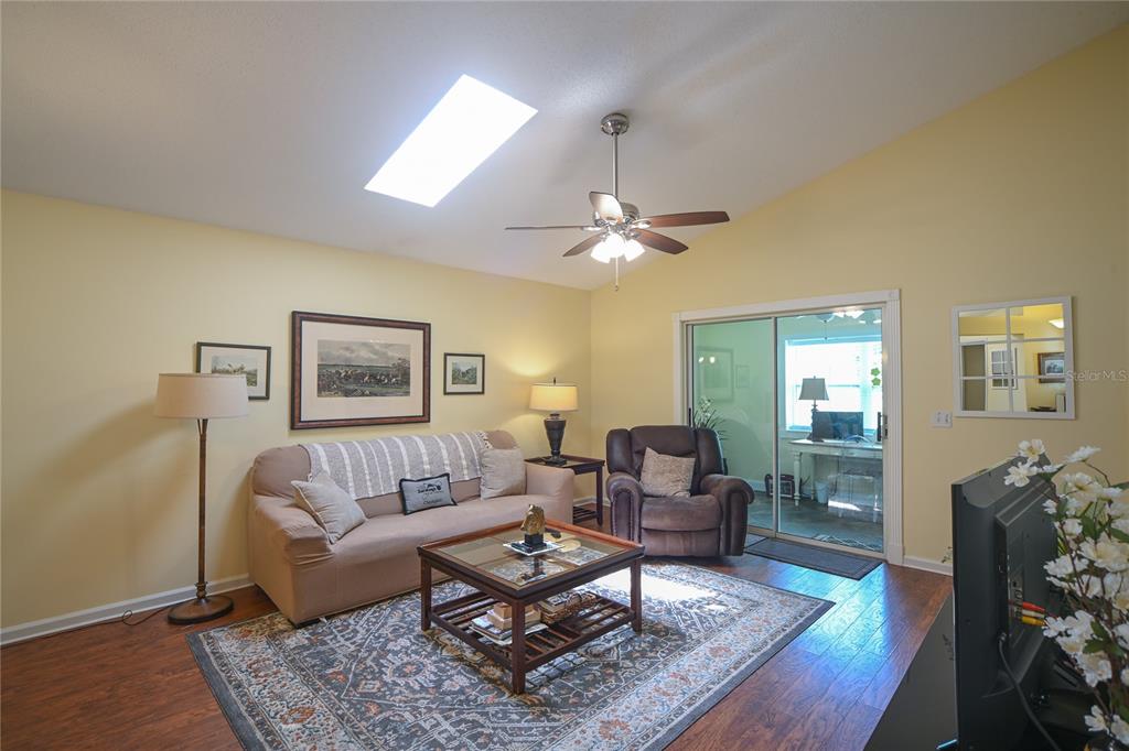 A living room with a vaulted ceiling, skylight, ceiling fan, and sliding glass doors — 1918 NW 50TH AVENUE, OCALA, FL