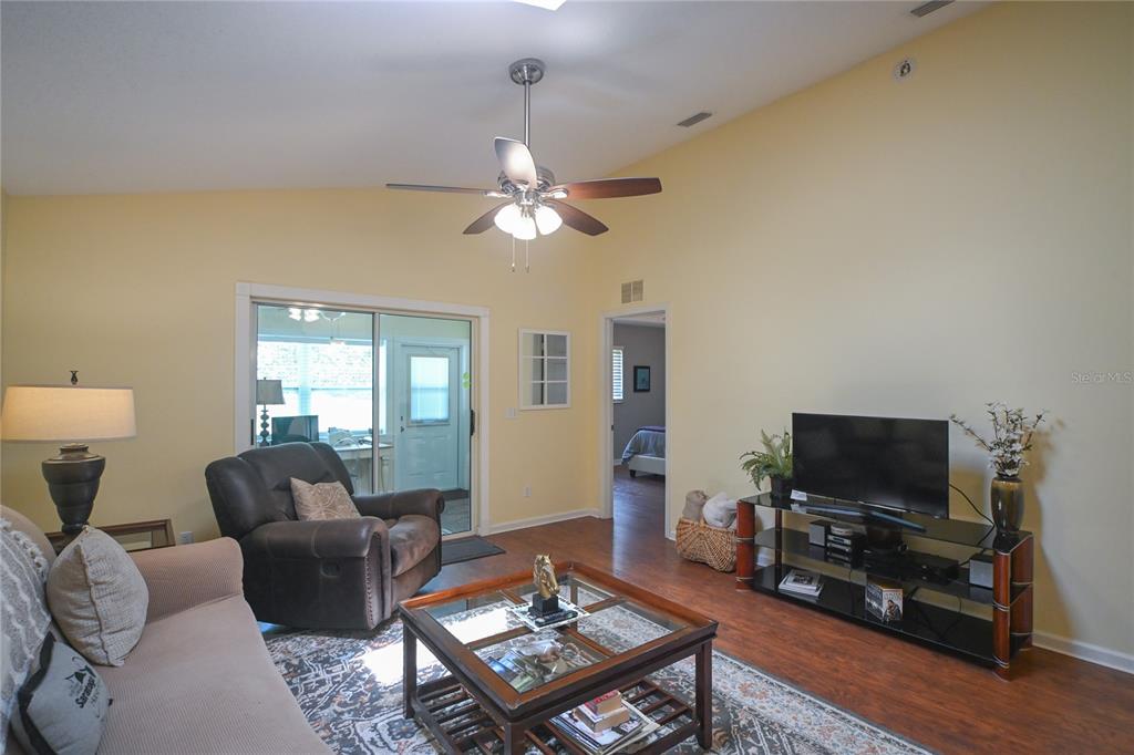 A living room features a vaulted ceiling, a ceiling fan, a television, and a sliding door — 1918 NW 50TH AVENUE, OCALA, FL