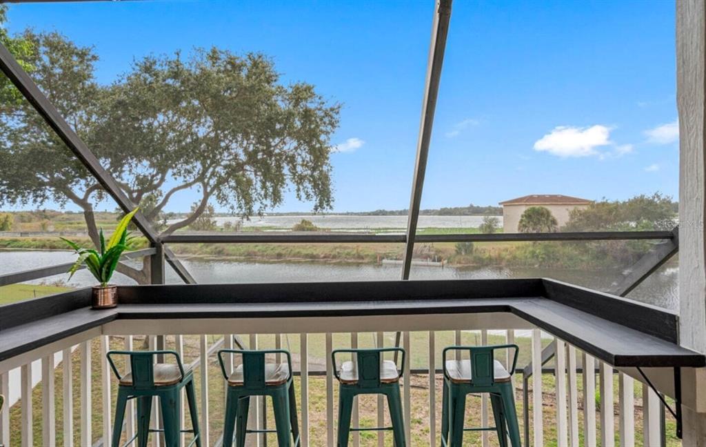 A screened-in balcony features a built-in bar counter with four stools overlooking a lake — 12692 PINEWAY DRIVE, LARGO, FL