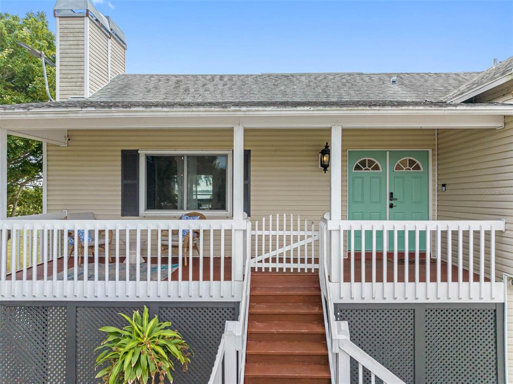 An elevated wooden deck with a staircase and a light green double front door — 12692 PINEWAY DRIVE, LARGO, FL