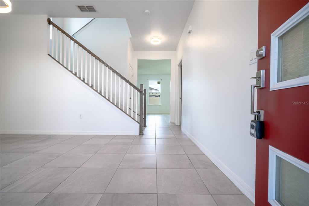 An entryway features light tile flooring, a staircase with a wooden railing, and a red door — 2510 AMATI DRIVE, KISSIMMEE, FL