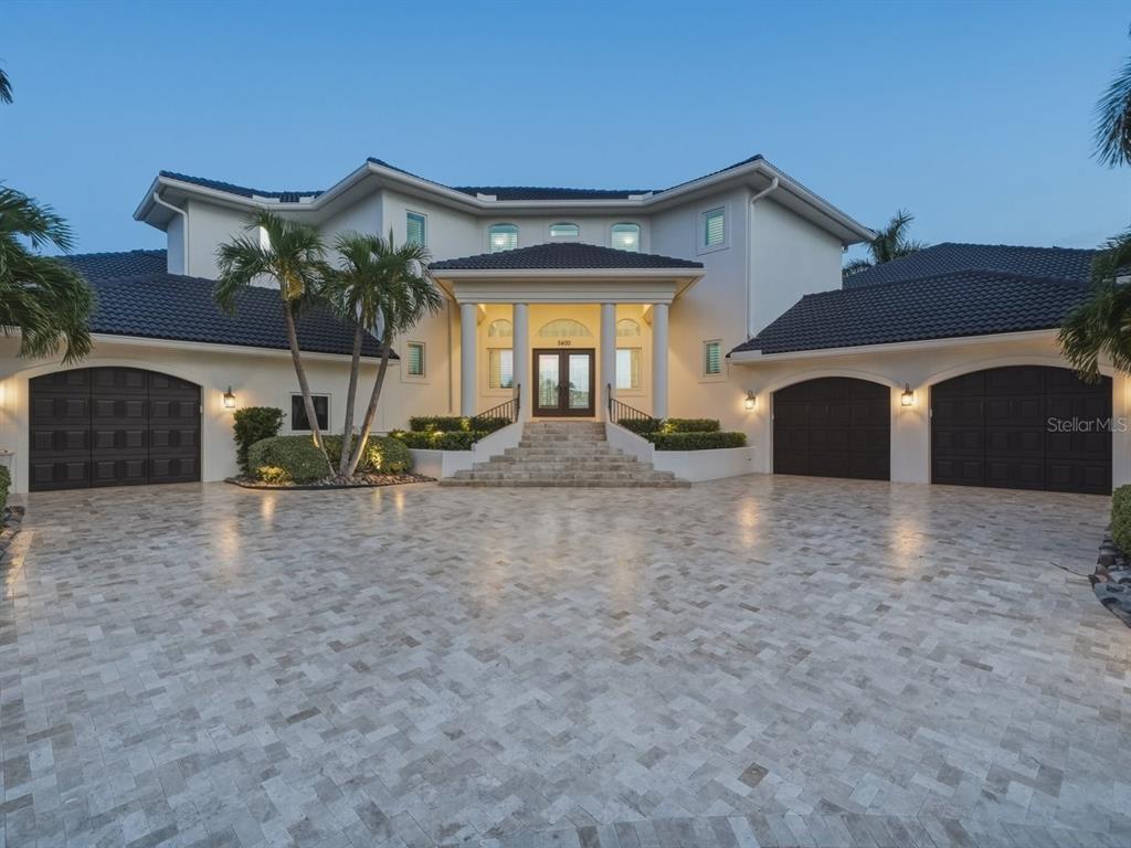 A large two-story house with a paved driveway, three garage doors, and a grand entrance staircase — 5400 PALI WAY, ST PETE BEACH, FL
