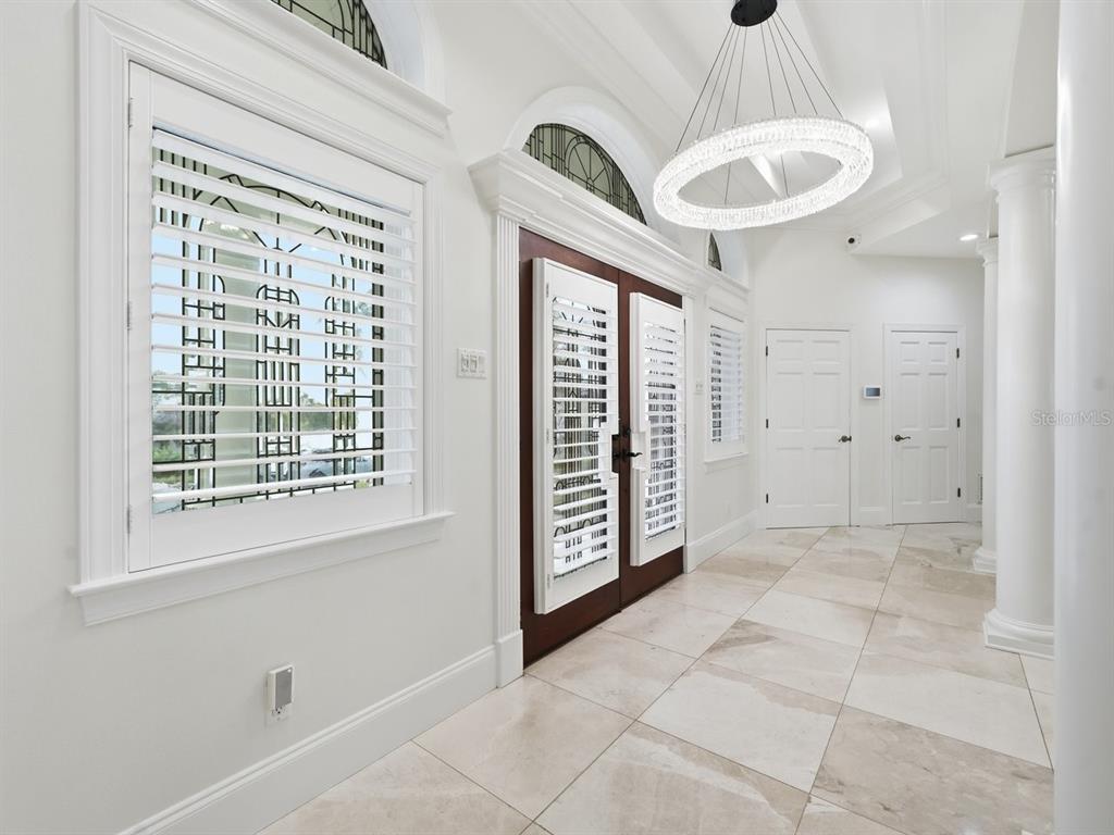 A bright entryway features white walls, tile flooring, a crystal chandelier, and double front doors — 5400 PALI WAY, ST PETE BEACH, FL