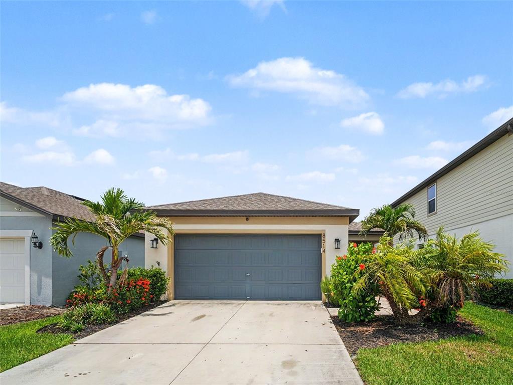 A single-story house exterior features a gray garage door, a concrete driveway, and palm trees — 8514 ABALONE LOOP, PARRISH, FL