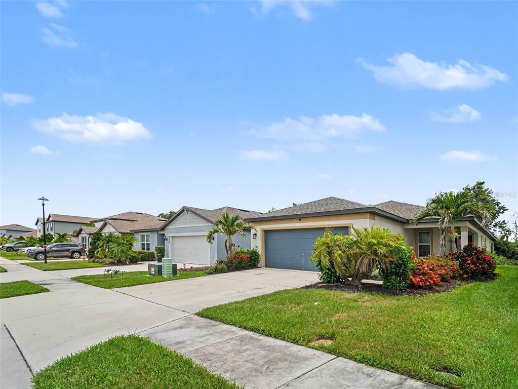 A street view of suburban single-family homes with driveways, lawns, and blue garage doors — 8514 ABALONE LOOP, PARRISH, FL