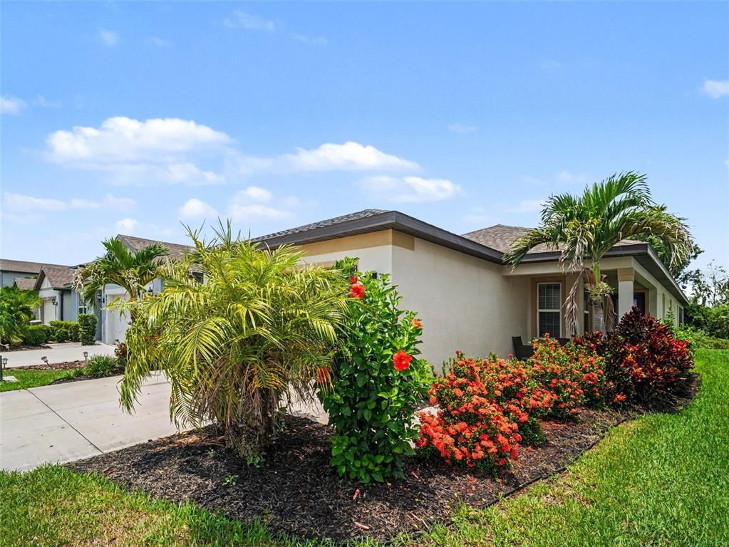 A single-story house exterior features a concrete driveway, palm trees, and flowering shrubs — 8514 ABALONE LOOP, PARRISH, FL