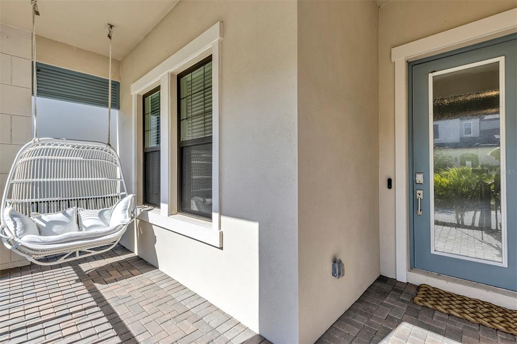 A covered porch features a hanging white wicker chair, two windows, and a blue door — 1115 SEAGRAPE DRIVE, RUSKIN, FL