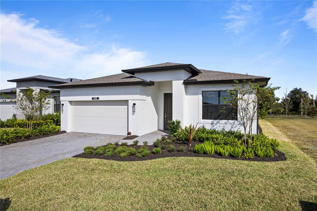 A modern single-story house with a white stucco exterior, a two-car garage, and landscaping — 5028 LOWLAND TERRACE, PARRISH, FL