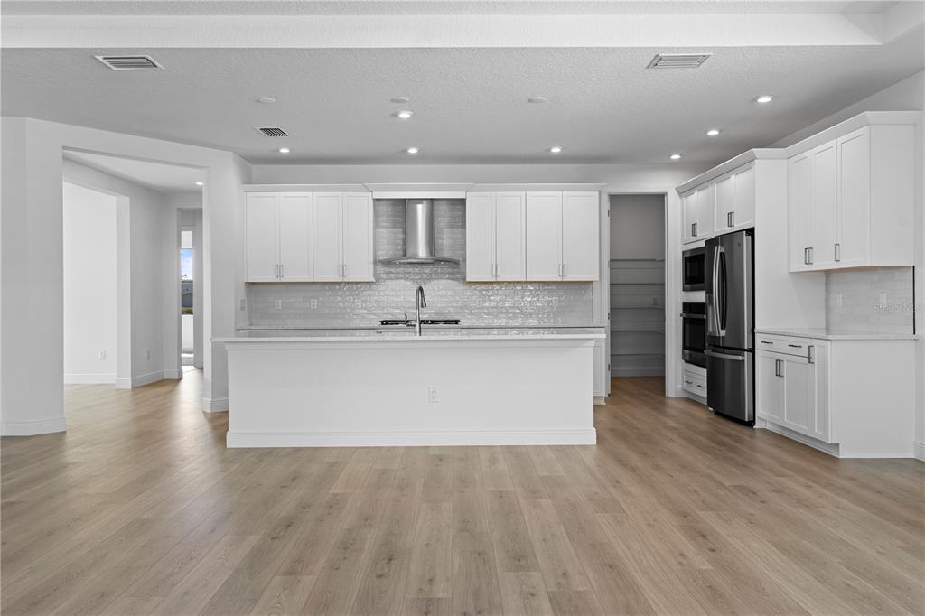 A modern kitchen features white cabinetry, a large island, stainless steel appliances, and wood flooring — 5028 LOWLAND TERRACE, PARRISH, FL