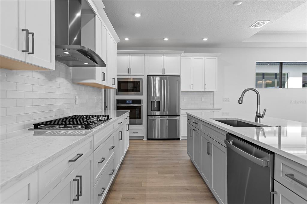 A modern kitchen features white cabinetry, stainless steel appliances, a large island, and light wood flooring — 5028 LOWLAND TERRACE, PARRISH, FL