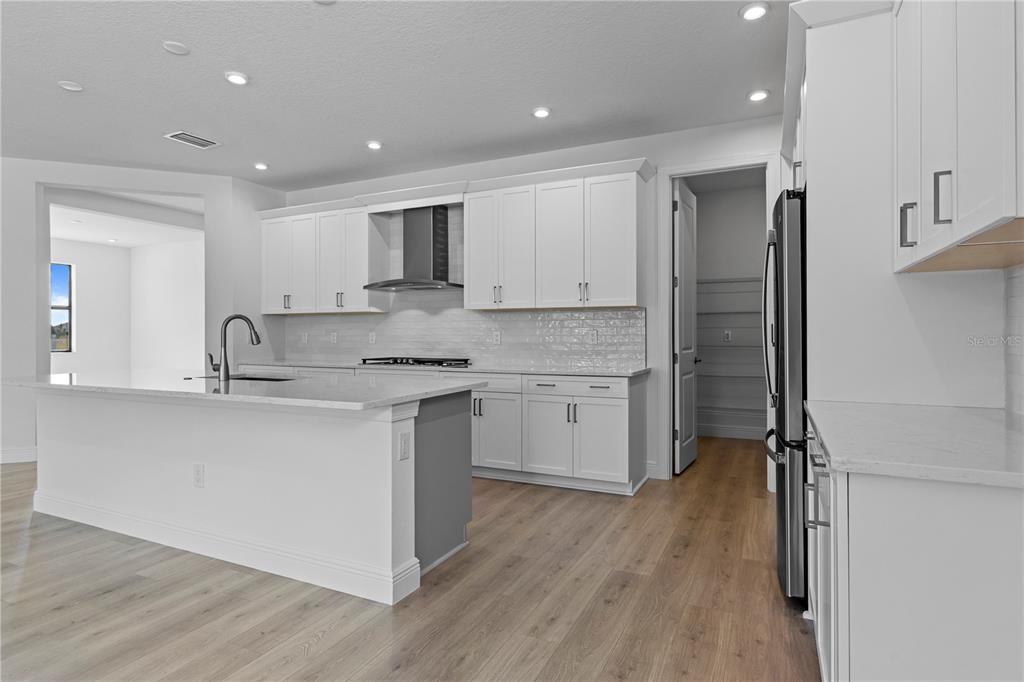 A modern kitchen features white cabinetry, a large island with a sink, and light wood flooring — 5028 LOWLAND TERRACE, PARRISH, FL