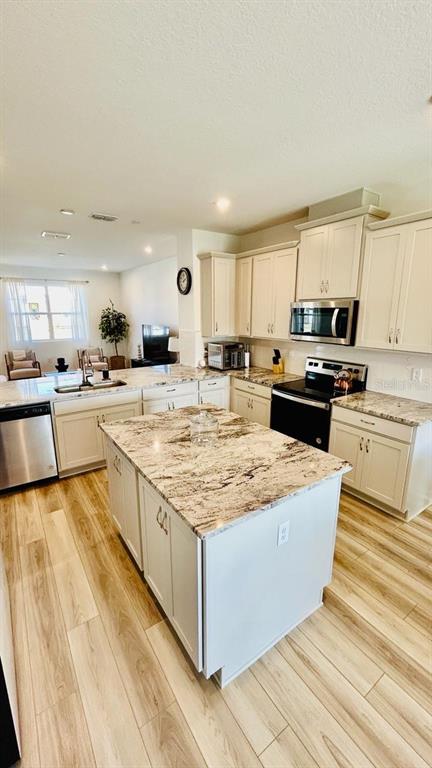 A kitchen features white cabinets, granite countertops, a central island, and light wood-look flooring — 11926 SUNSAIL AVENUE, ORLANDO, FL