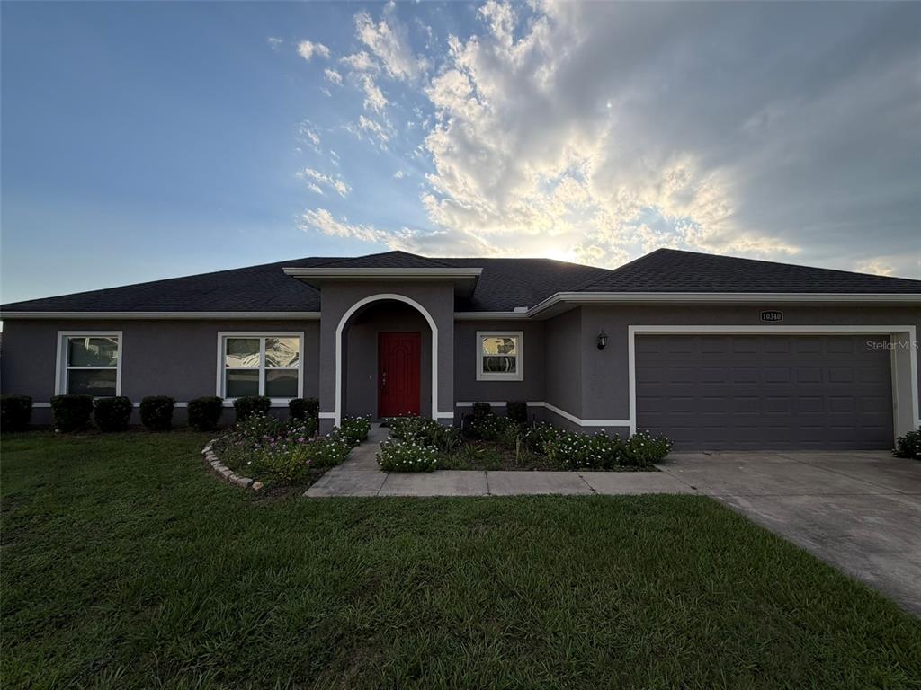 A gray single-story house features a red front door, a garage, and a landscaped yard — 10340 SE 69TH TERRACE, BELLEVIEW, FL