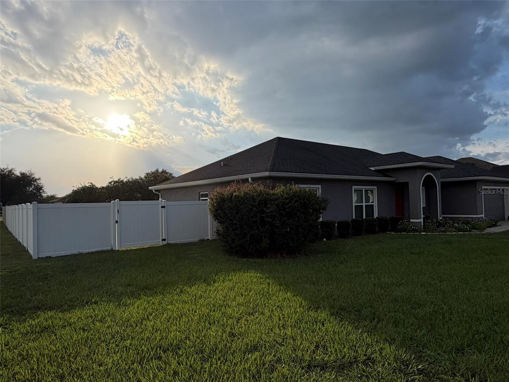A gray house with a white vinyl fence stands under a cloudy, sunlit sky — 10340 SE 69TH TERRACE, BELLEVIEW, FL