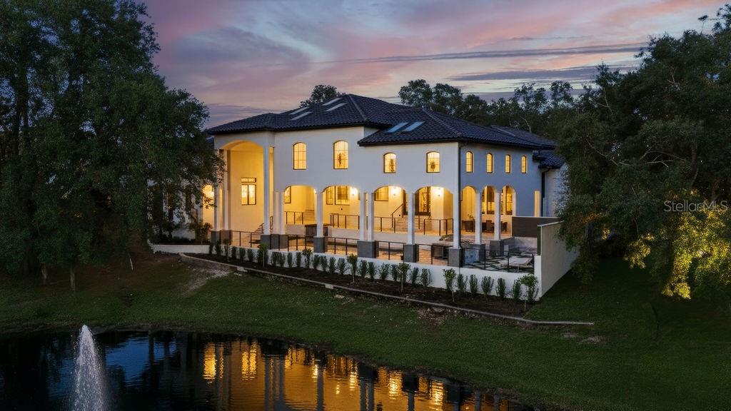 An exterior view of a large two-story house with arched columns overlooking a pond — 9725 CHESTNUT RIDGE DRIVE, WINDERMERE, FL