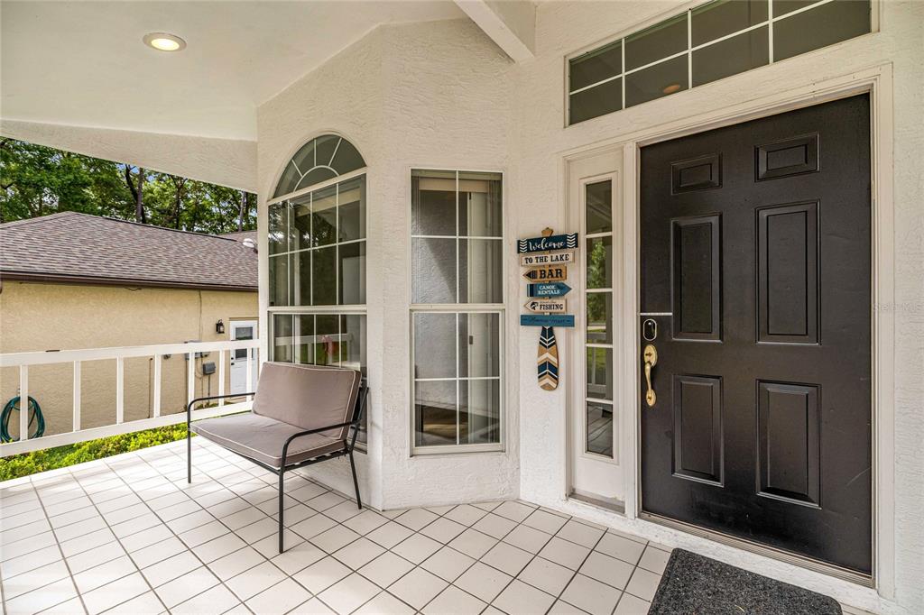 A covered porch features a tiled floor, a bench, and a black front door — 19195 SW 92ND LOOP, DUNNELLON, FL