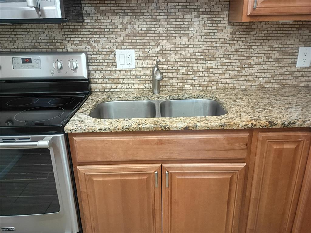 A kitchen features light wood cabinets, granite countertops, stainless steel appliances, and a tiled backsplash — 1520 GLEN OAKS DRIVE E UNIT 248, SARASOTA, FL